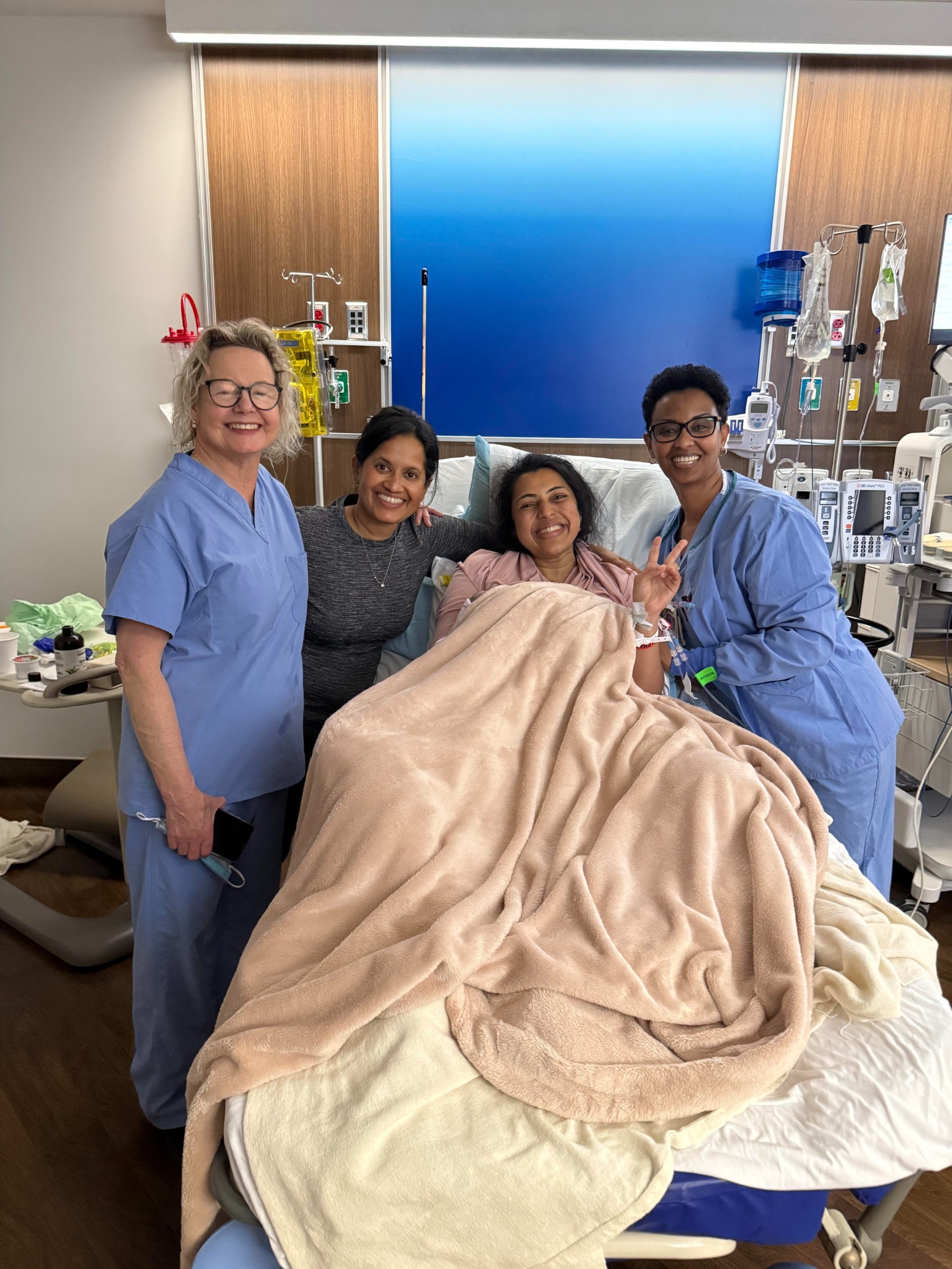 Four adults together beside a hospital bed